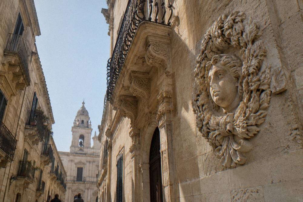 Detailed carved limestone wreath and face on a church wall in Lecce