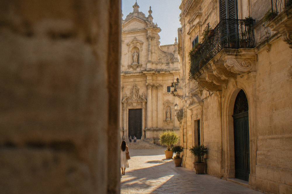 A honey-stone baroque church facade with ornate carved details in a southern Italian street