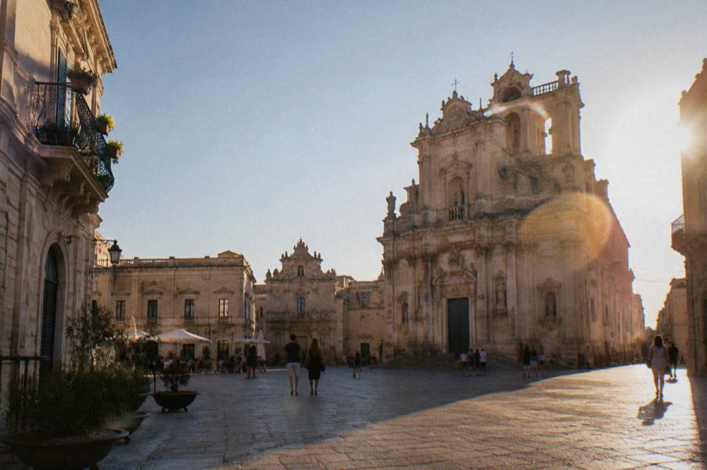 A sunlit square in a baroque southern Italian town with warm stone facades under a clear sky