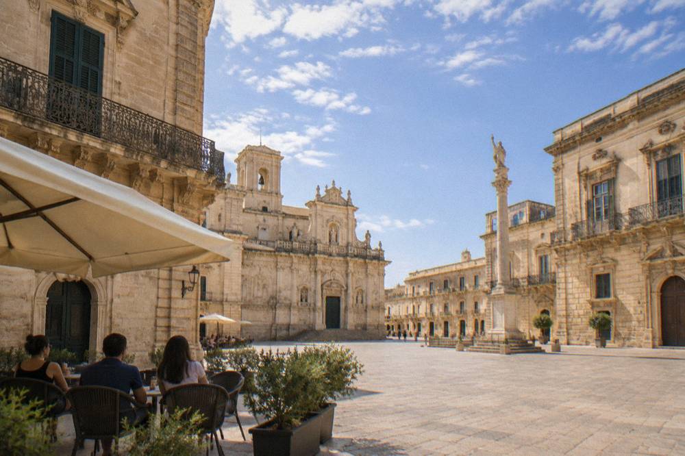 People sitting in the shade at an outdoor table in a Lecce square in summer