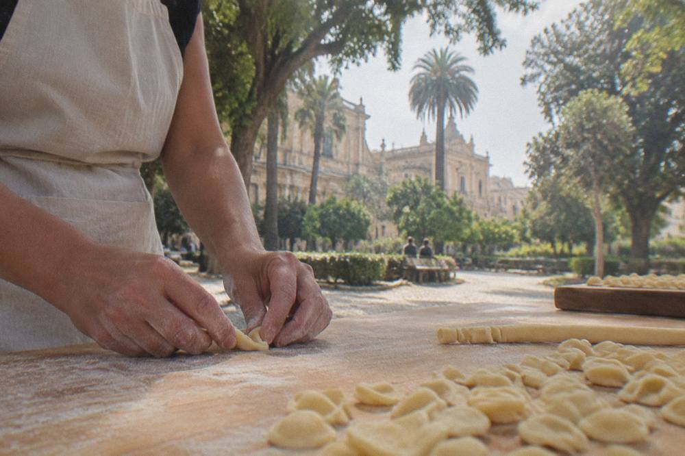 Hands shaping fresh pasta dough on a wooden table during a cooking class