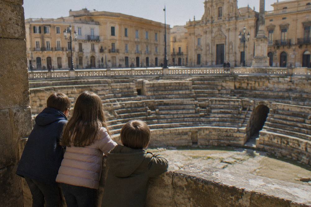 Children looking down into the sunken Roman amphitheatre from a Lecce square