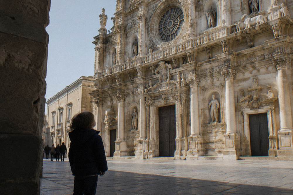 A child looking up at the ornate facade of the Basilica di Santa Croce in Lecce