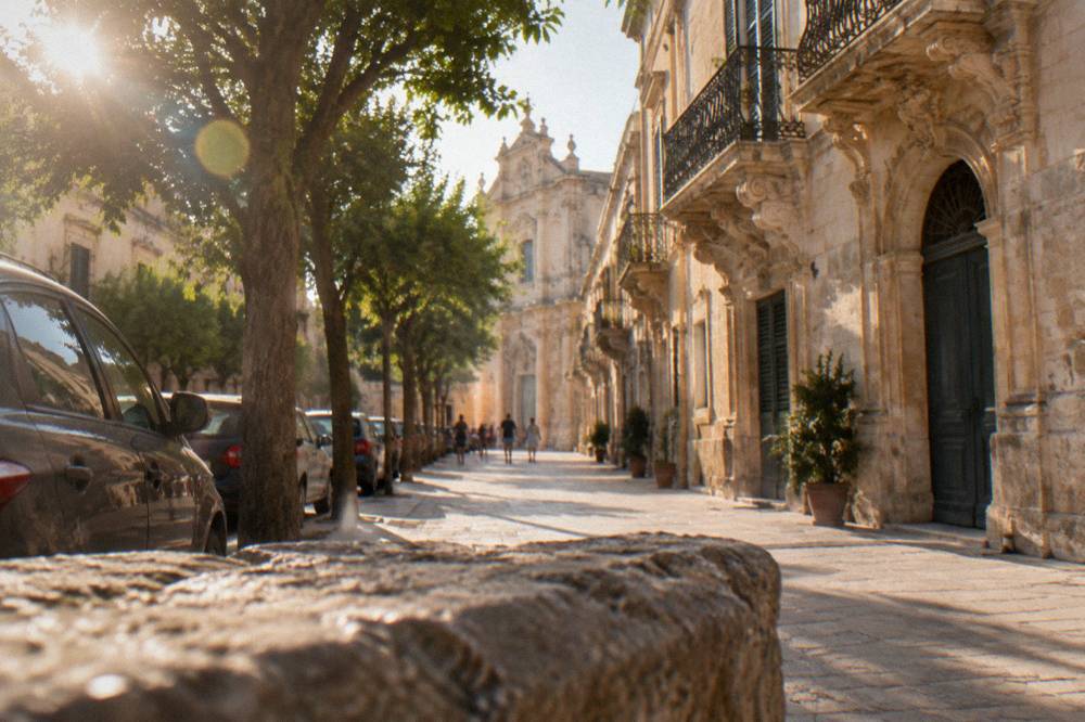 Cars parked in a row along a tree-lined street on the edge of Lecce's old town