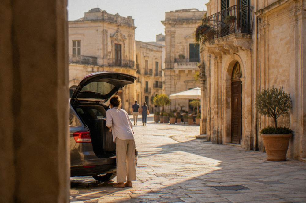 A guest suitcase being unloaded from a car boot on a sunlit street in Lecce