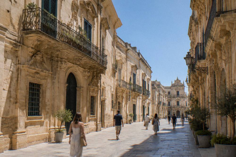 Pedestrians walking past ornate baroque facades in a car-free Lecce street