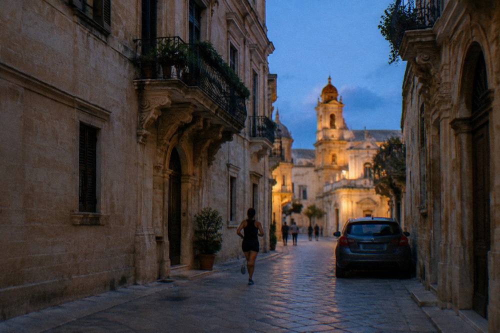 A parked car with the walled skyline of Lecce's old town glowing in evening light behind it