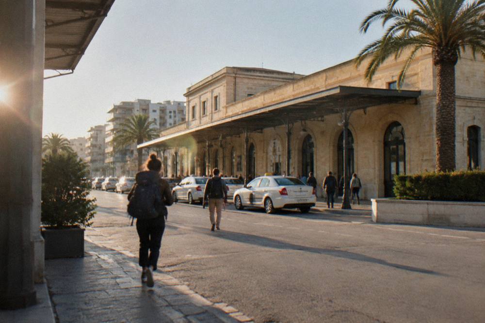 Facade of Lecce railway station with taxis waiting and people carrying backpacks