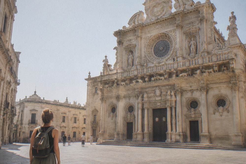 Traveller with a small daypack facing the ornate facade of Basilica di Santa Croce in Lecce