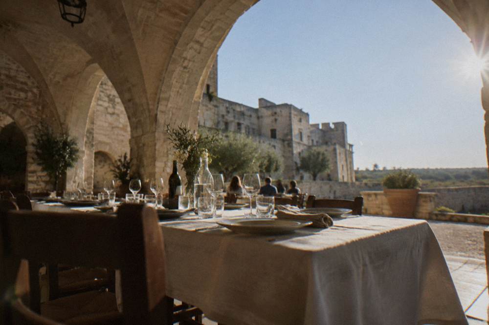 A long table set for lunch under stone vaults in a farmhouse courtyard