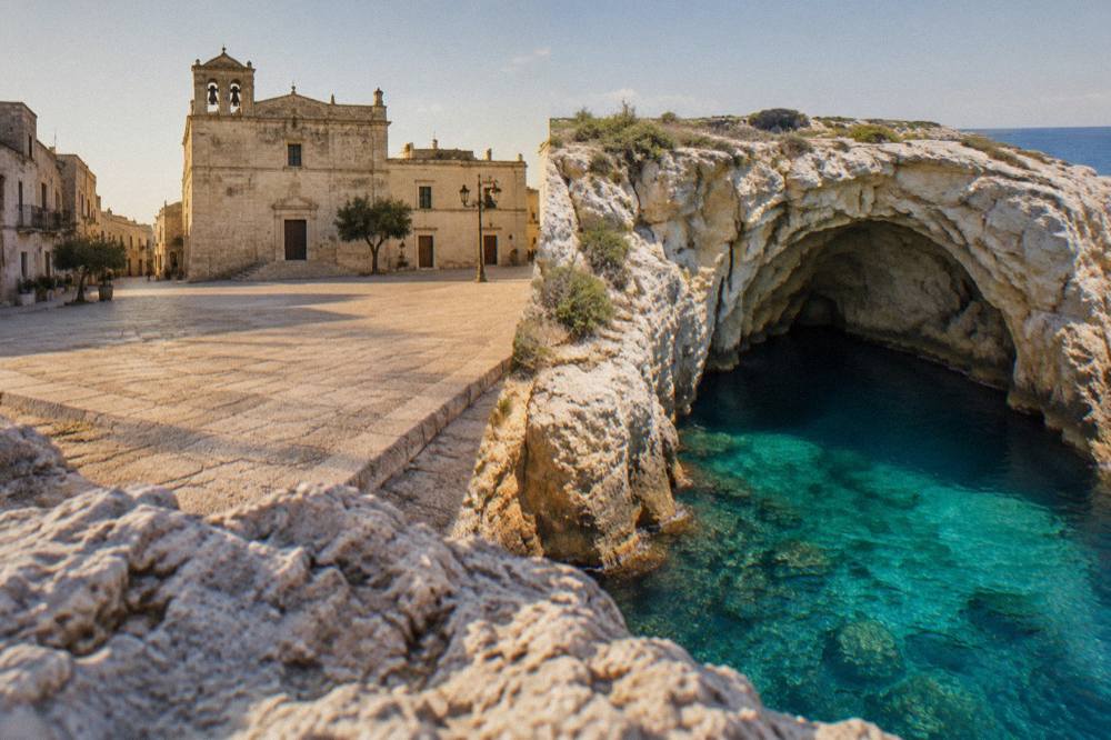 An aerial view of a turquoise sea cave surrounded by limestone rocks on the Salento coast