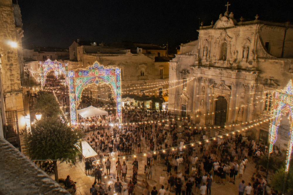 Strings of festival lights and illuminations over a crowded square at night in a southern Italian town