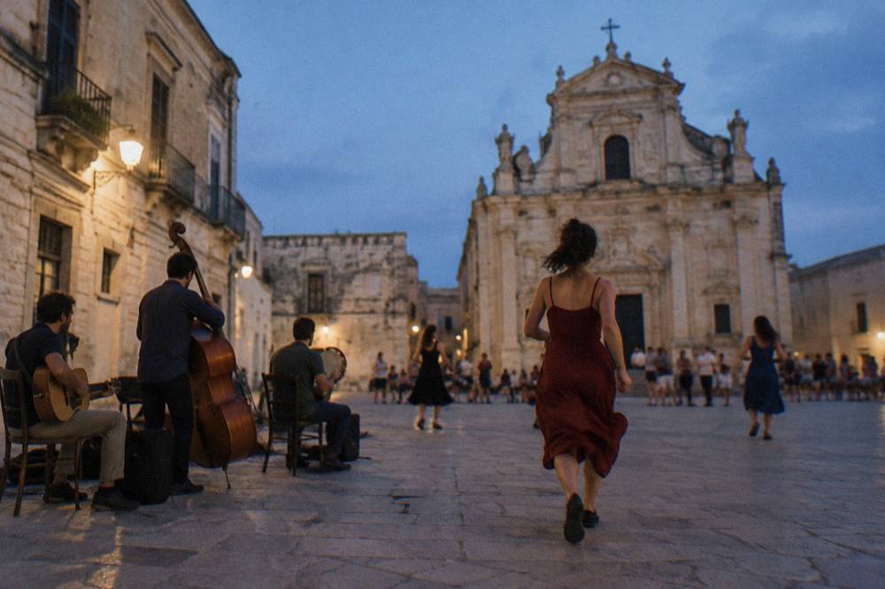 Dancers and musicians performing outdoors at dusk in a small piazza surrounded by old stone buildings