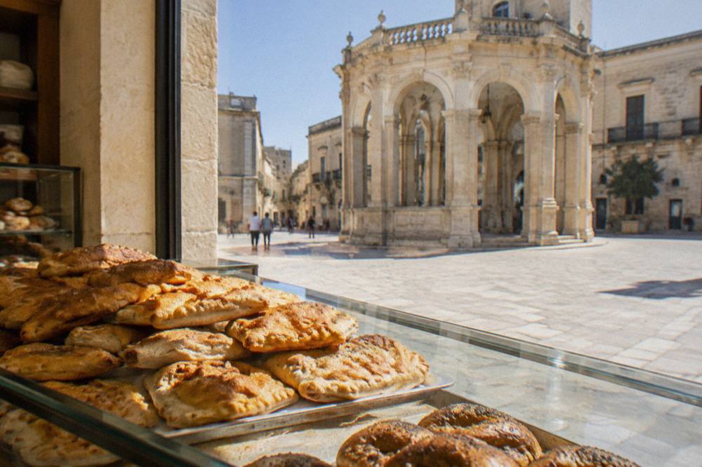 Stack of baked rustico pastries behind a glass bakery counter in a Lecce pastry shop
