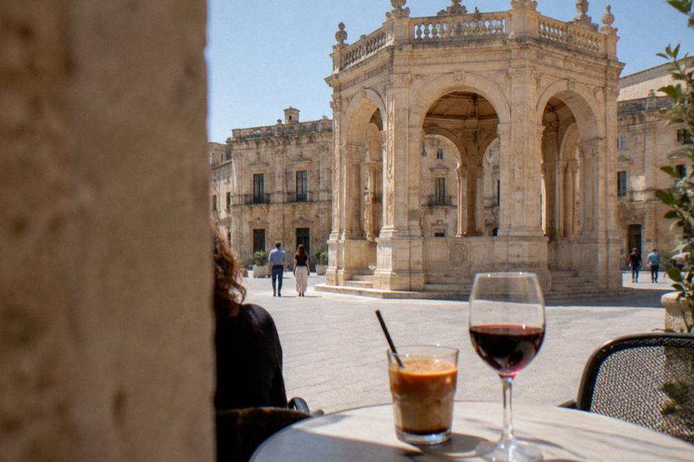 Glass of iced espresso with almond milk beside a glass of red Salento wine on an outdoor table
