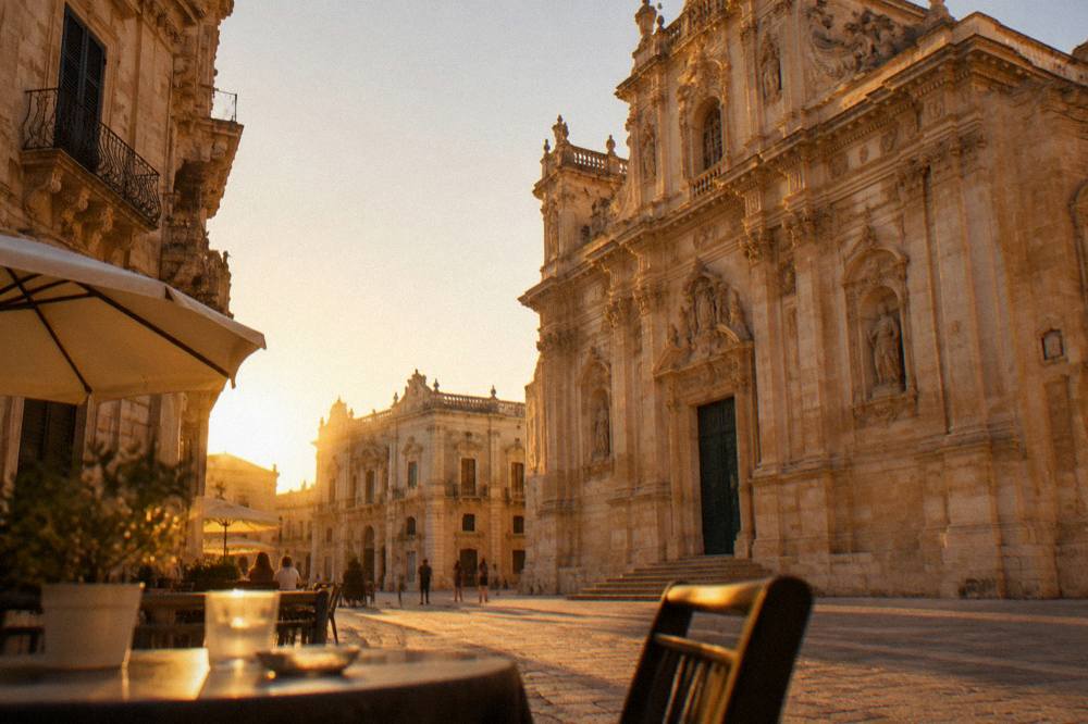 Evening view of a Lecce square with café tables and baroque facades lit by warm light
