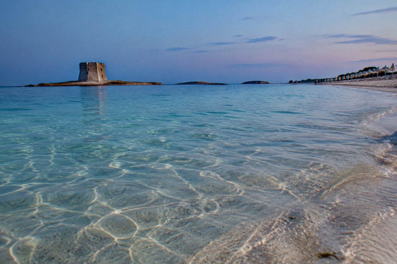 A sandy Salento beach with clear shallow water and a row of sun umbrellas