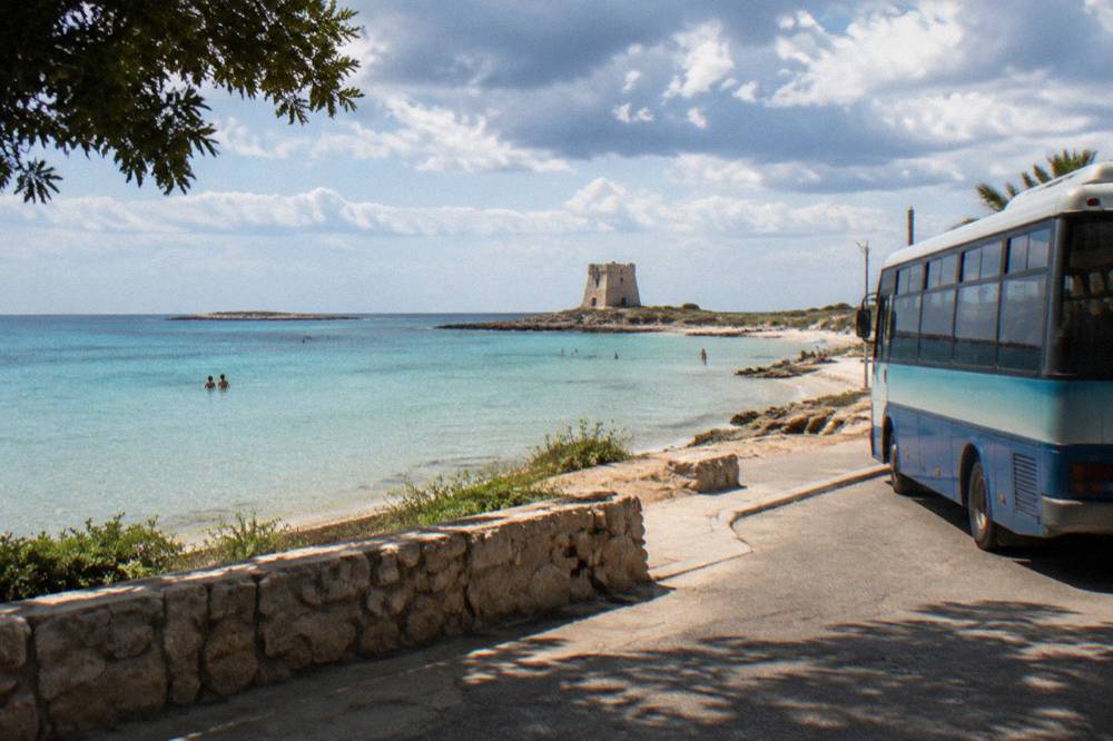 A regional bus parked at a seaside stop in a small Salento beach town