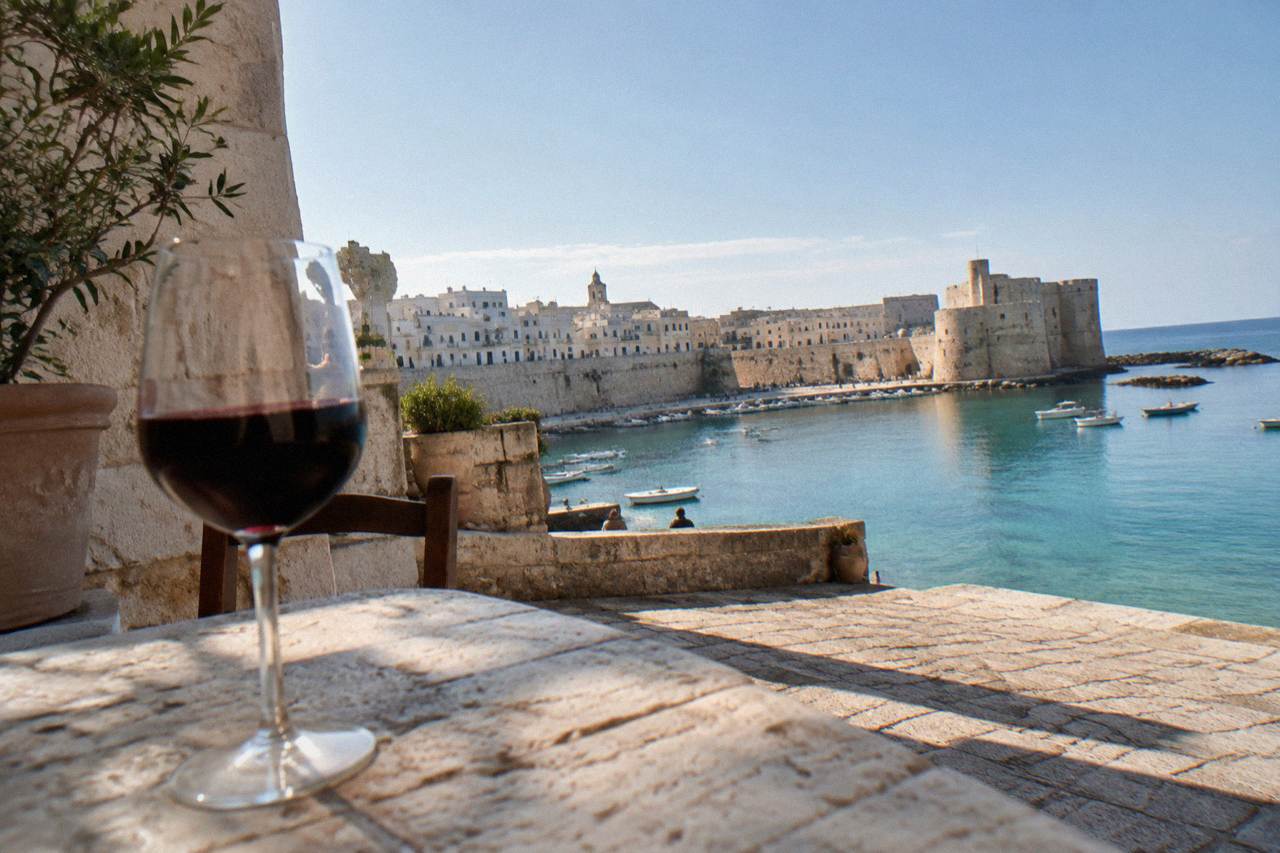 A glass of dark red wine on a sunlit stone table in a southern Italian courtyard