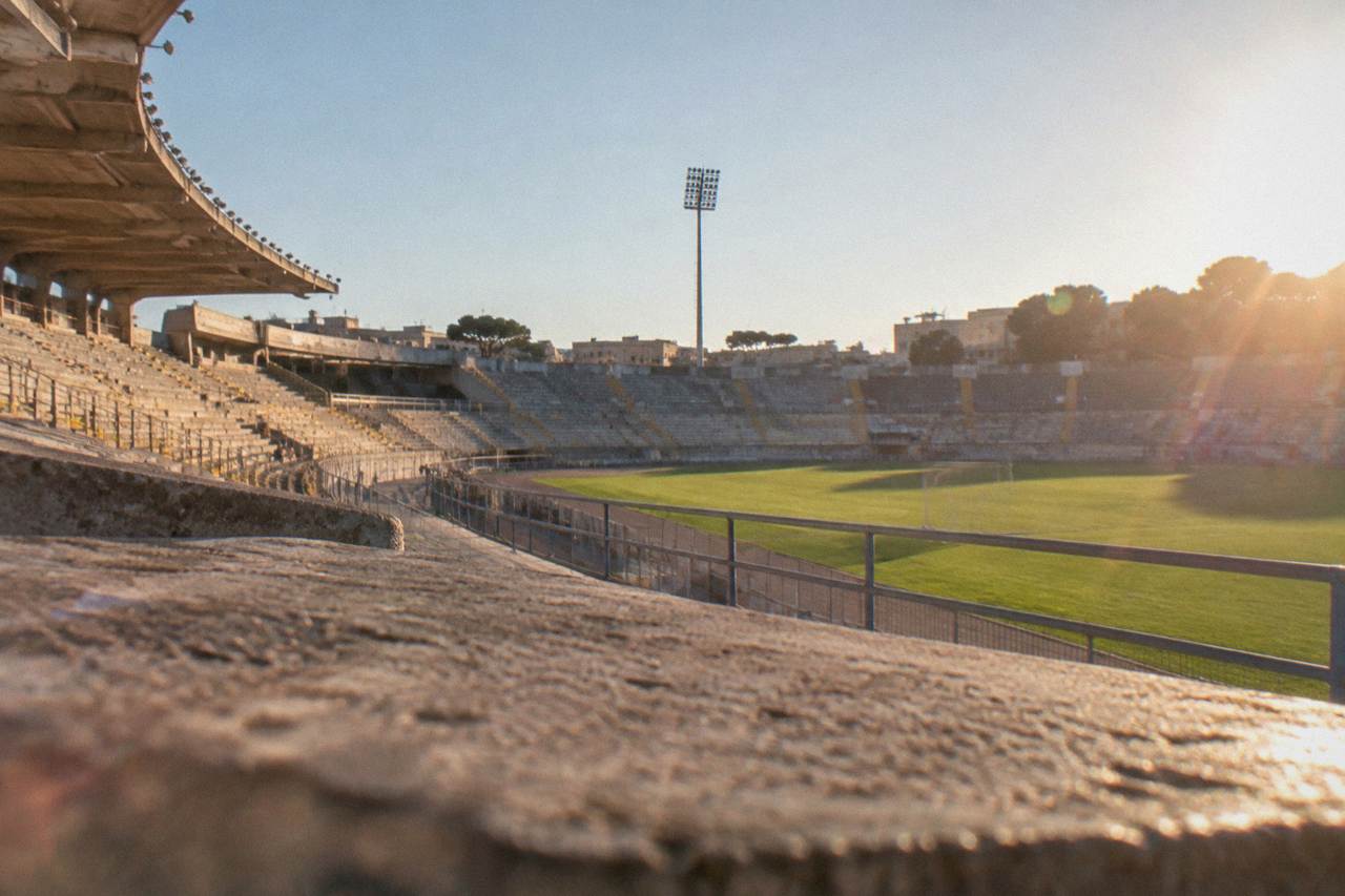 A football stadium bowl on the edge of a southern Italian town under a clear afternoon sky