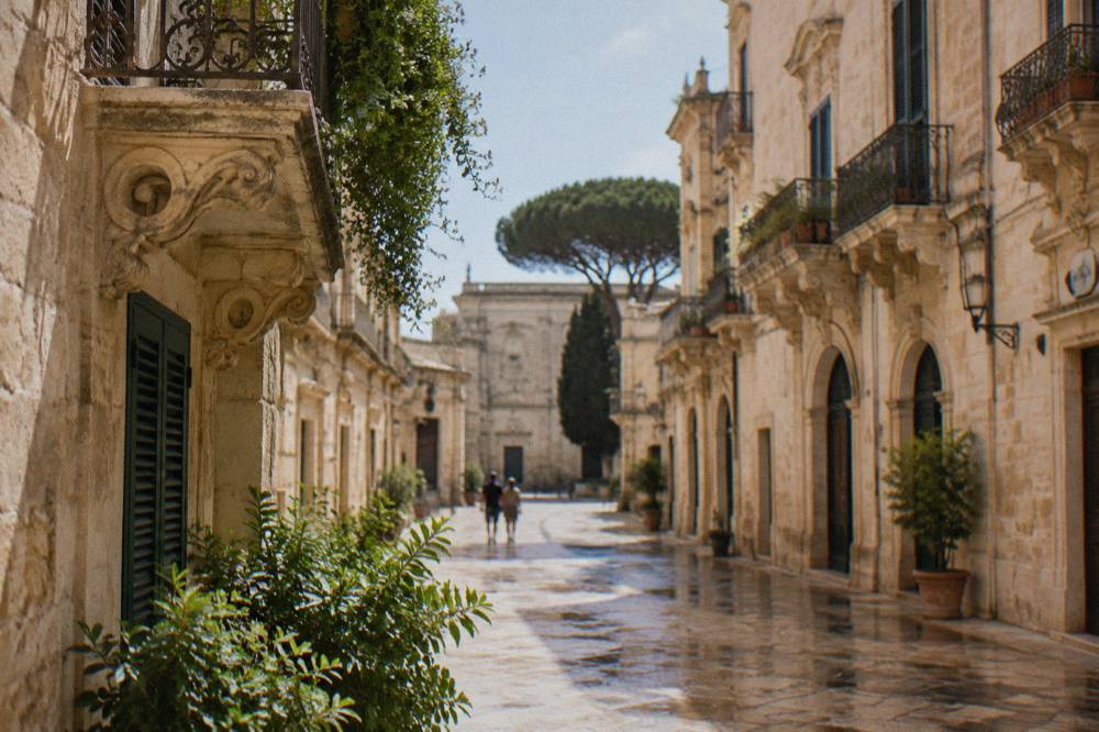 A wide residential boulevard in a southern Italian city lined with apartment blocks and stone pines