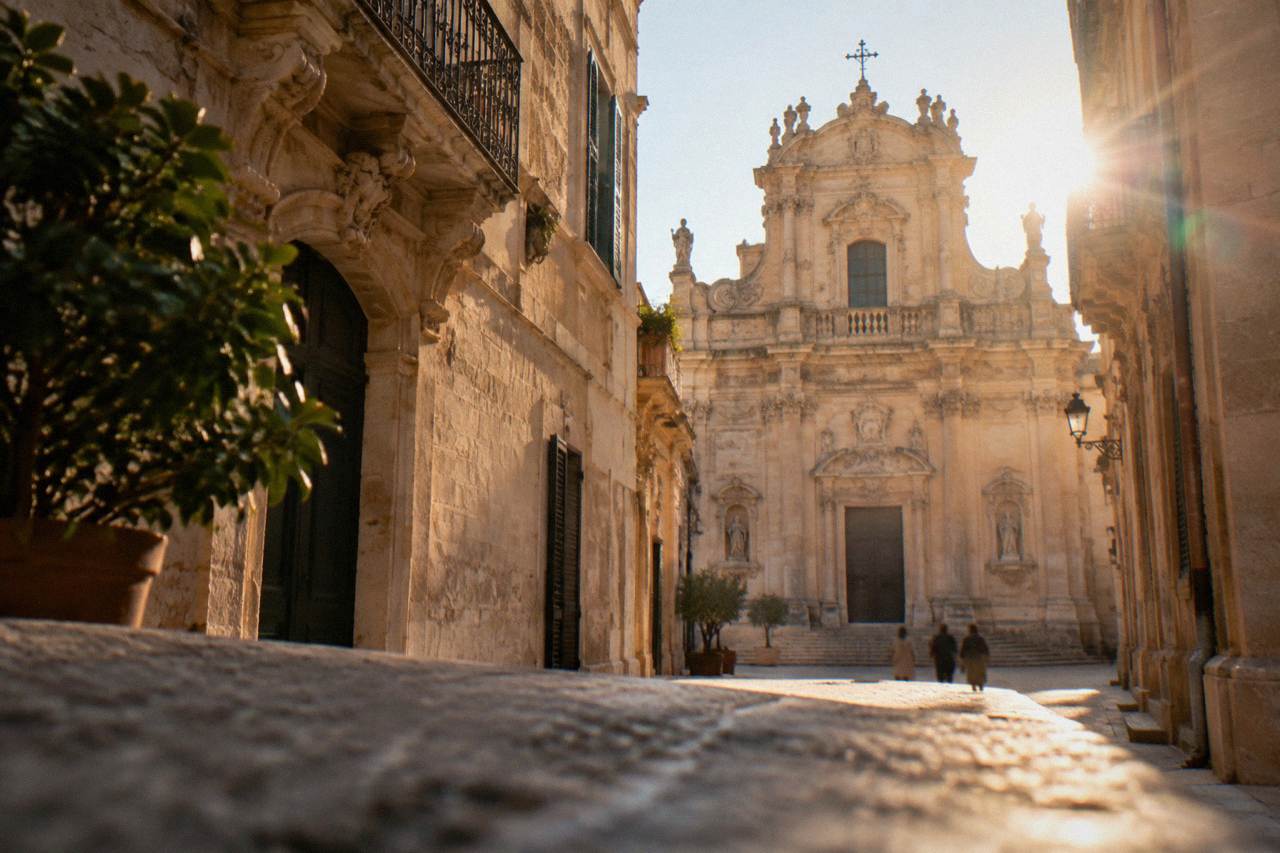 A honey-coloured baroque church facade in Lecce seen from a narrow street in warm afternoon light