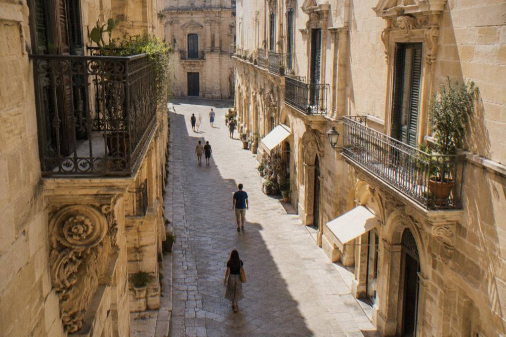 A narrow Lecce street lined with warm limestone palazzi and small shops in late morning light