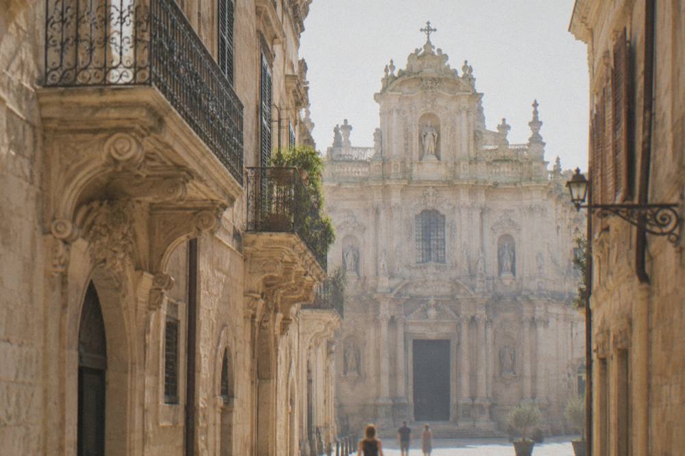 The ornate facade of a baroque church in Lecce seen from a narrow street