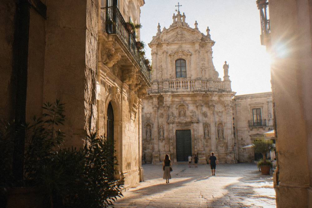 The ornate carved facade of a baroque church in Lecce seen from a narrow square