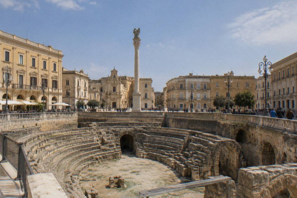 A busy square in Lecce with a Roman amphitheatre excavation below the pavement and a column at its centre.