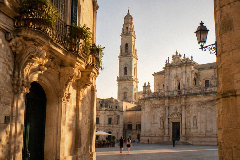 The cathedral in Lecce seen from its enclosed piazza, with a tall bell tower beside it.