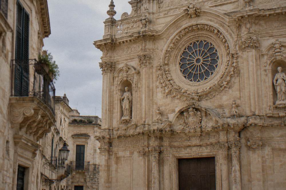 A carved baroque church facade in golden limestone with a detailed rose window.